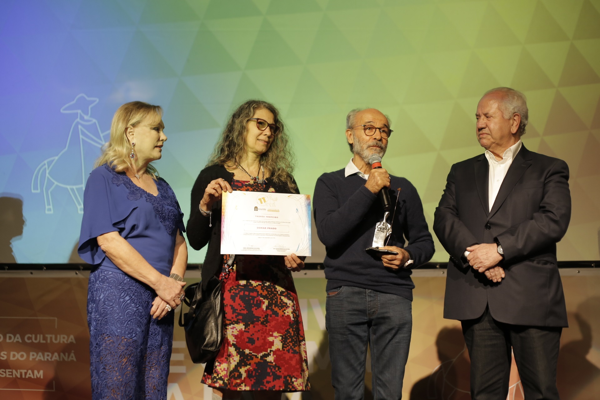 O ator Osmar Prado (ao microfone), vencedor do prêmio de Melhor Ator (pelo filme 10 Segundos para Vencer, a cinebiografia de Eder Jofre), acompanhado pela mulher, Vânia Pacheco (de vermelho), e pelo casal Maria Inês e Luiz Carlos Borges da Silveira, idealizadores do Festival de Cinema da Lapa.
